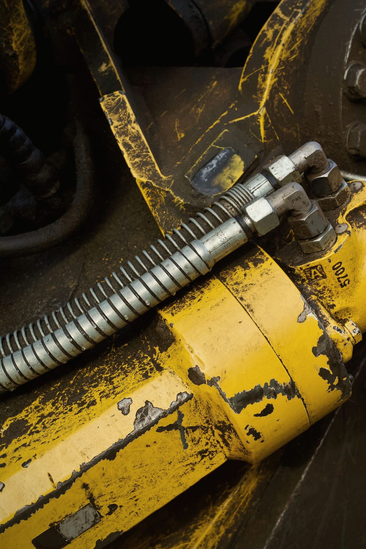 A yellow hydraulic cylinder barrel with a hose line and hex fitting