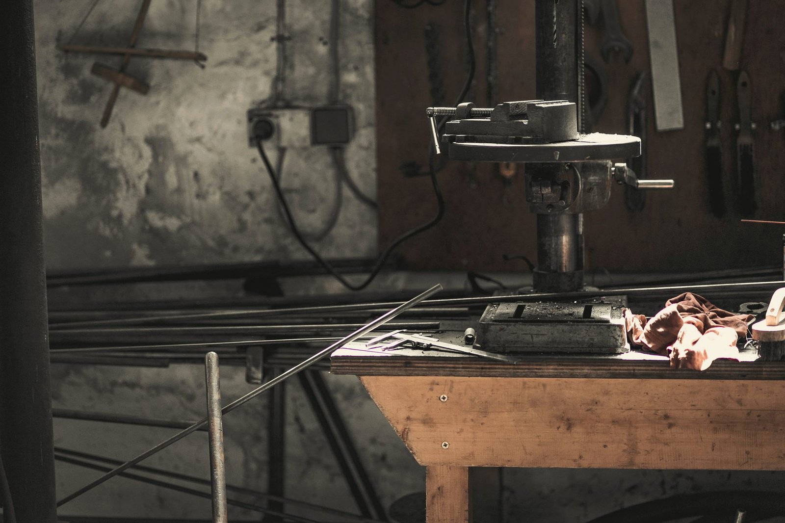 A drill press over a steel bench with bar stock laid out