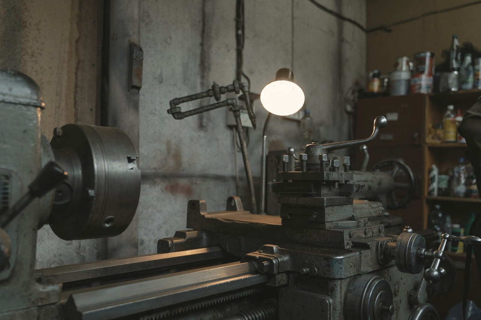 A lathe lit by a single hanging lamp in a workshop