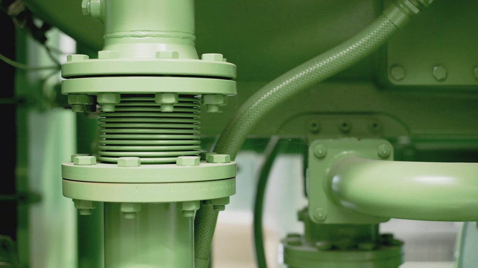 A green painted valve and pipe run on industrial plant equipment